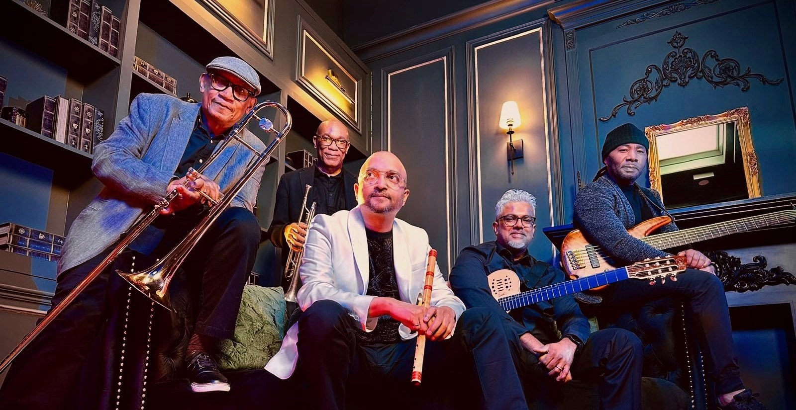 Flute Siva with the band, seated on a sofa with trombone, trumpet, guitar and bass
