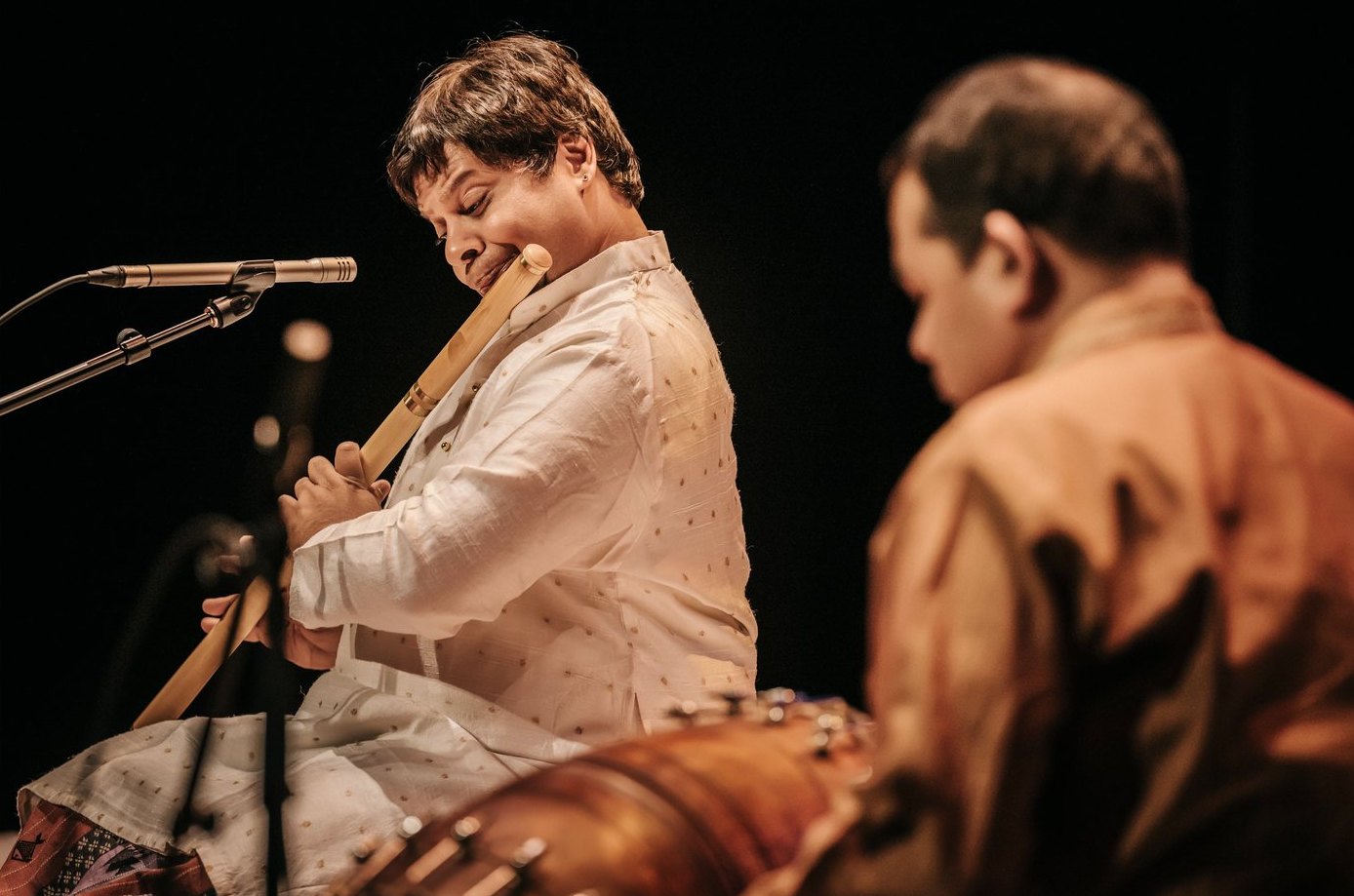 Maestro Shashank Subramanyam playing the flute on stage, with the mridangam artist in the foreground
